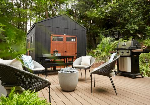 Compass Big Sky with black siding and brown double doors in a backyard with an outdoor table, grill, seating, and fire ring.